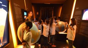 Descrição da imagem: Crianças observando painéis. A esquerda e direita, maquetes do globo terrestres. 
